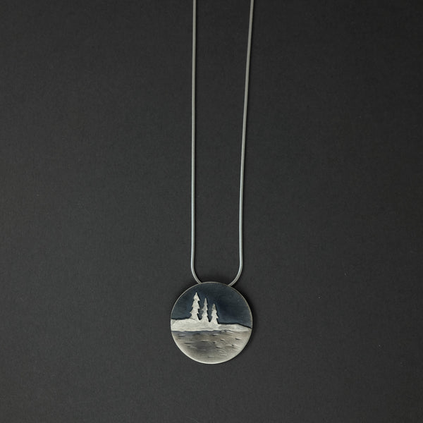 pendant necklace depicting three pine tress, a shoreline and a body of water